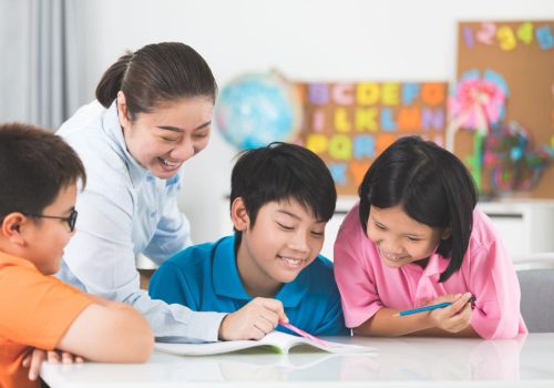 young-asian-teacher-helps-young-school-kids-class-1.jpg